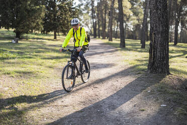 Glücklicher Mann, der einen Helm trägt und an einem sonnigen Tag Fahrrad fährt - JCCMF10881