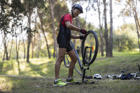 Happy man repairing bicycle tire in forest - JCCMF10894