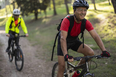 Lächelnder Mann auf dem Fahrrad mit einem Freund im Wald - JCCMF10897