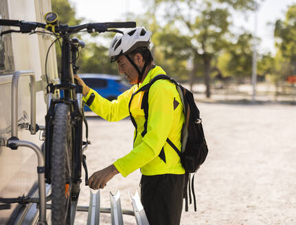 Älterer Mann trägt einen Helm und stellt sein Fahrrad auf einem Lieferwagen ein - JCCMF10902