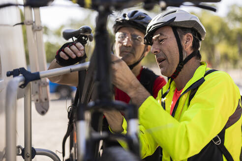 Mature friends adjusting bicycle on van - JCCMF10904
