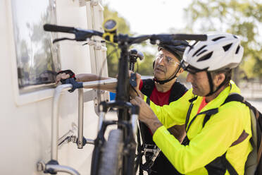 Freunde tragen einen Helm und stellen ihr Fahrrad hinter einem Lieferwagen ab - JCCMF10905
