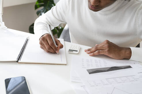 Young businessman sitting at desk and working on documents in home office - ALKF00774