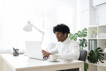 Focused businessman wearing wireless in-ear headphones working on laptop at desk - ALKF00782