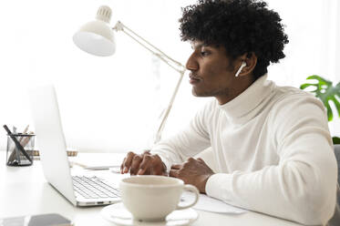 Businessman sitting at desk and working on laptop in home office - ALKF00786