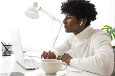 Geschäftsmann sitzt am Schreibtisch und arbeitet an einem Laptop im Büro zu Hause - ALKF00786
