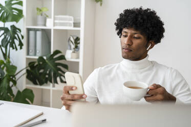 Geschäftsmann mit einer Tasse Tee in der Hand und einem Smartphone im Heimbüro - ALKF00789