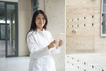 Smiling scientist standing with tablet PC in corridor - JOSEF21871