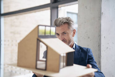 Mature businessman examining model house in office - JOSEF21932