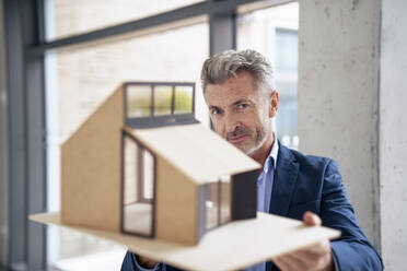 Mature businessman standing with model house in office - JOSEF21933