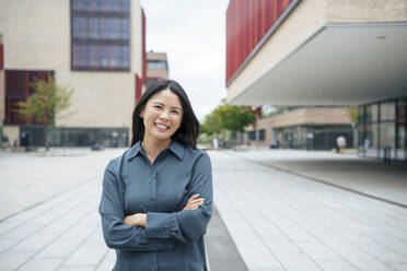 Smiling businesswoman standing with arms crossed near buildings - JOSEF21939