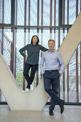 Businessman with businesswoman standing on architectural column - JOSEF21970