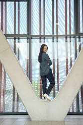 Smiling businesswoman with long black hair standing on architectural column - JOSEF21974