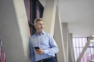 Mature businessman with smart phone leaning on columns - JOSEF21983