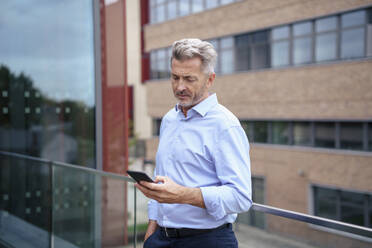 Businessman using smart phone near railing on balcony - JOSEF22012