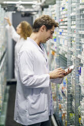 Apotheker mit Tablet-PC in der Nähe des Medikamentenregals in der Apotheke - JSMF02900