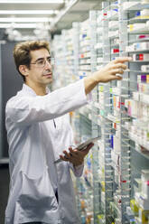 Pharmacist wearing eyeglasses holding tablet PC and taking inventory at pharmacy - JSMF02901