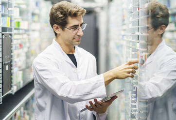 Pharmacist examining medicine stock on shelves at pharmacy - JSMF02902