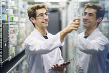 Lächelnder Chemiker, der einen Tablet-PC hält und Medikamente in einer Apotheke untersucht - JSMF02903