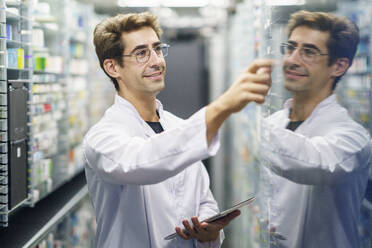 Smiling chemist holding tablet PC and examining medicine at pharmacy - JSMF02903