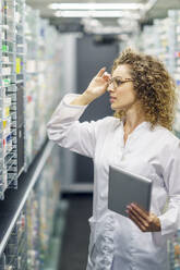 Pharmacist wearing eyeglasses and examining medicine at shelves in pharmacy - JSMF02905