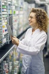 Smiling chemist examining and taking inventory through tablet PC in pharmacy - JSMF02907