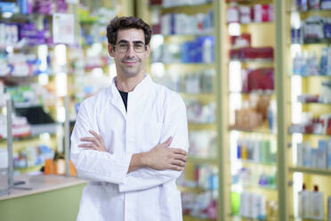 Smiling pharmacist with arms crossed at pharmacy - JSMF02919