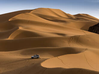 Aerial View of an off road vehicle driving among the sand dunes at sunset in the Sahara desert, Djanet, Algeria, Africa. - AAEF22942