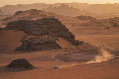 Luftaufnahme eines Autos inmitten von Sanddünen mit Felsformationen bei Sonnenuntergang in der Wüste Sahara, Djanet, Algerien, Afrika. - AAEF22957