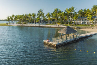 Aerial view of a woman sitting on the pier along the coastline, Poste de Flacq, Flacq district, Mauritius. - AAEF23247