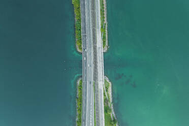 Aerial view of vehicles driving on a road crossing the Lugano lake, Melide, Ticino, Switzerland. - AAEF23475