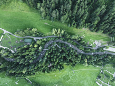 Aerial view of a small river among trees along the mountain crest in Ortisei, a small village on the Dolomites Trentino, South Tyrol in Northern Italy. - AAEF23540