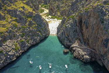 Luftaufnahme des Strandes Sa Calobra mit Booten und Menschen, die im klaren blauen Wasser zwischen dem engen felsigen Tal des Torrent de Pareis auf den Balearen, Spanien, schwimmen. - AAEF23811