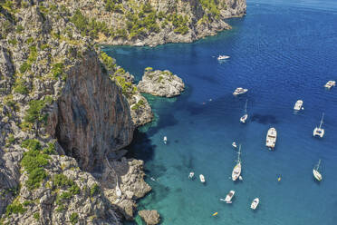 Aerial view of boats, yachts and sailboats in clear blue waters next to a rocky mountain by Sa Calobra beach in Balearic Islands, Spain. - AAEF23816