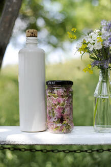 Weiße Flasche, Glas mit Schnittlauchblüten und blühender Blumenstrauß auf einer Bank - GISF00988