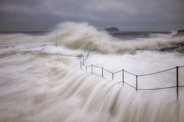 UK, Scotland, North Berwick, Long exposure of waves splashing against coastal railing during Storm Babet - SMAF02636