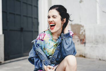 Young woman wearing denim jacket and laughing near wall - SVCF00394