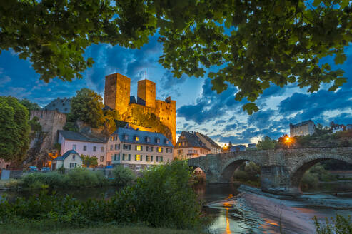 Germany, Hesse, Runkel, Arch bridge and houses in front of Runkel Castle at dusk - MHF00737