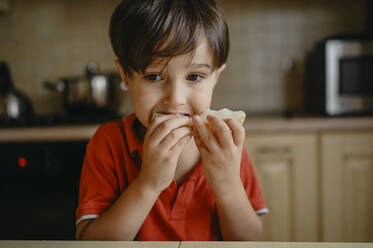 Junge trägt rotes Hemd und isst Melone zu Hause - ANAF02398