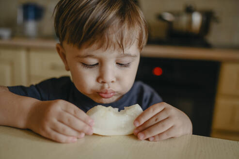 Junge isst ein Stück Melone am Tisch - ANAF02399