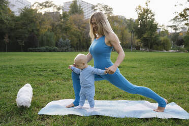 Lächelnde Mutter und Sohn beim Yoga mit Hund im Park - YBF00284
