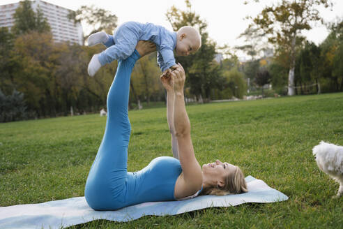 Playful mother and son doing yoga near dog in park - YBF00286