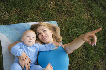 Glückliche Mutter gestikuliert und liegt mit ihrem Sohn auf einer Übungsmatte im Park - YBF00292
