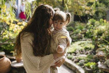 Liebevolle Mutter trägt und umarmt Tochter Garten - YBF00303