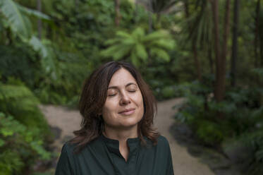 Smiling woman with eyes closed in botanical garden - VRAF00217