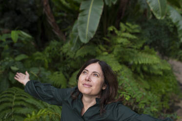 Smiling woman with arms outstretched in botanical garden - VRAF00218