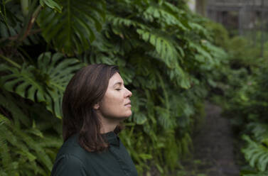 Woman with eyes closed in botanical garden - VRAF00223