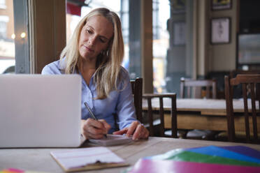 Blonde Freiberuflerin macht sich Notizen am Laptop in einem Café - ASGF04692