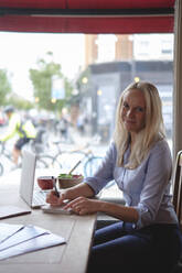 Lächelnder Freiberufler mit Notizblock und Laptop auf dem Tisch in einem Café - ASGF04693