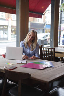 Blonde Freiberuflerin macht sich Notizen am Laptop im Café - ASGF04694